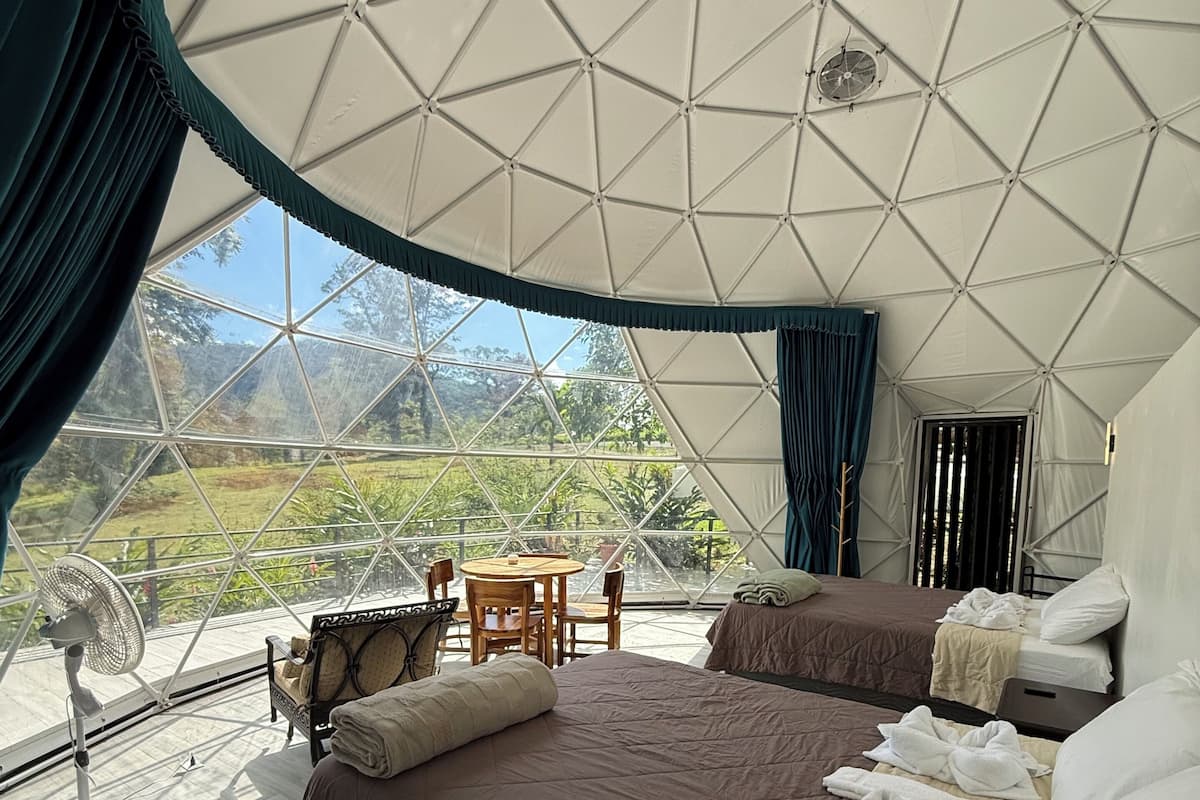 Un alloggio in tenda con due letti, un tavolo, sedie, un ventilatore e vista sulla natura.