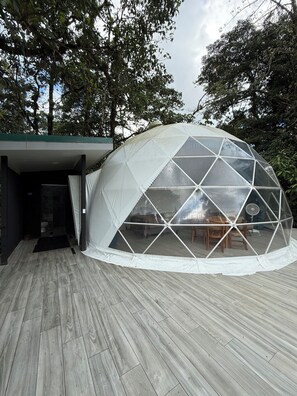 Une structure en forme de dôme géodésique, dotée d’une terrasse en bois et d’une entrée abritée.