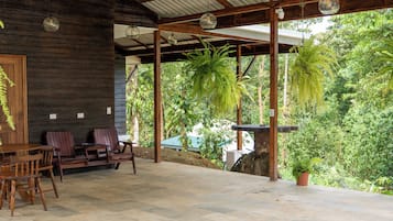 An outdoor patio area with a wooden bench, a table, and hanging ferns.