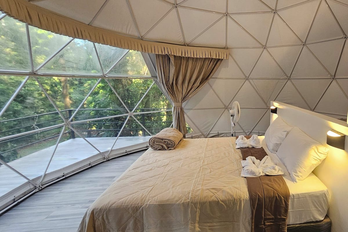 Una camera a tenda con un letto, una ventola e vista sul verde circostante.