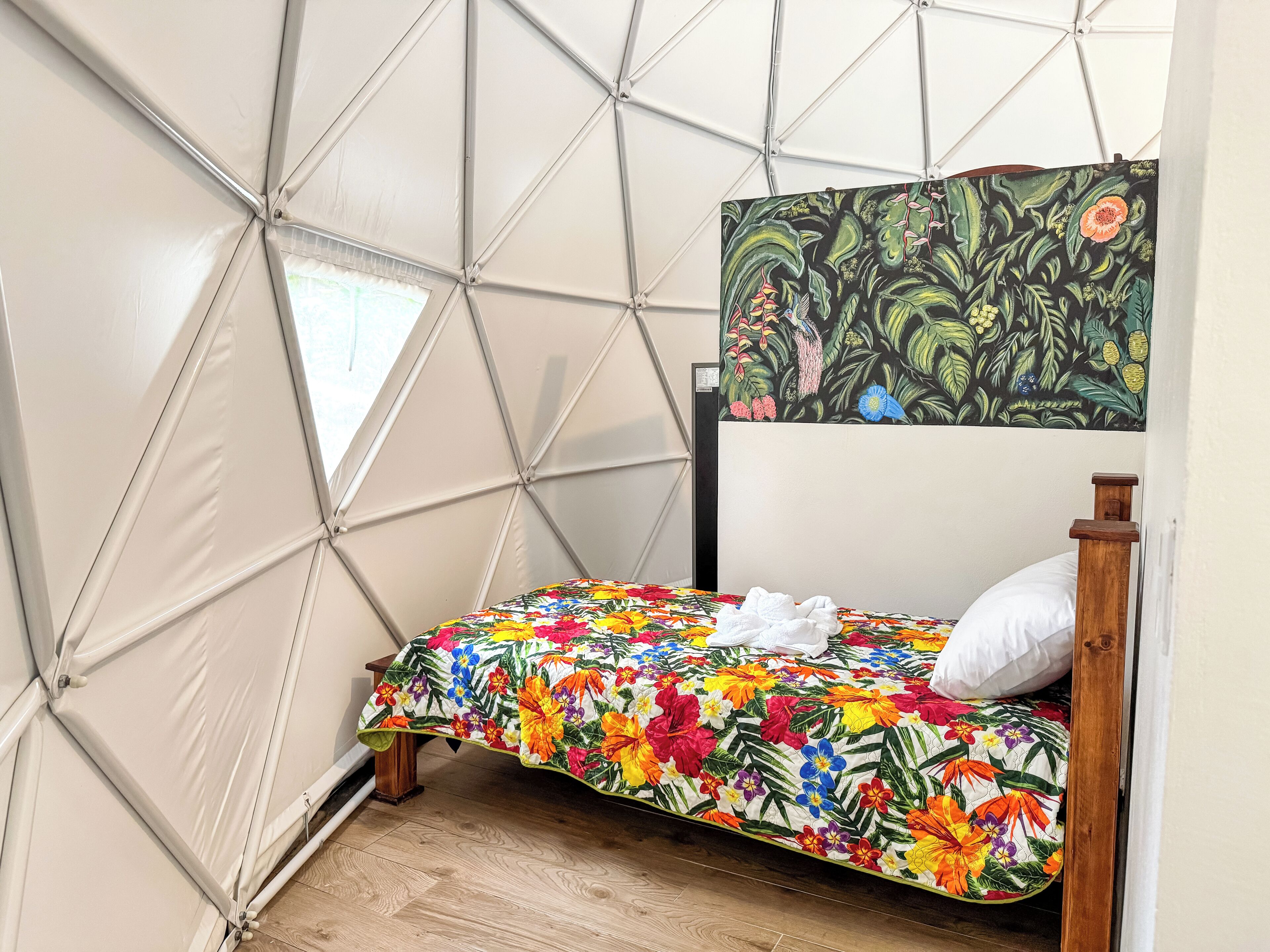 A small, enclosed room with a bed, a window, and a wall with a geometric pattern.