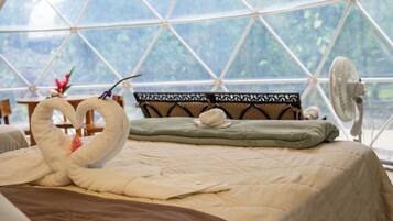 A bed with a quilted bedspread, two towels arranged in a heart shape, a green pillow, and a decorative pillow with a black and white pattern.