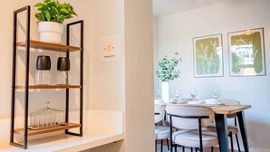 Un coin repas avec une table dressée pour quatre personnes, une plante en pot et des œuvres d’art encadrées accrochées au mur.