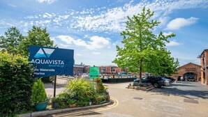 L’entrée d’une marina, avec une enseigne indiquant « Aquavista », un bâtiment en briques portant l’inscription « Brasserie Piston », et des voitures garées.