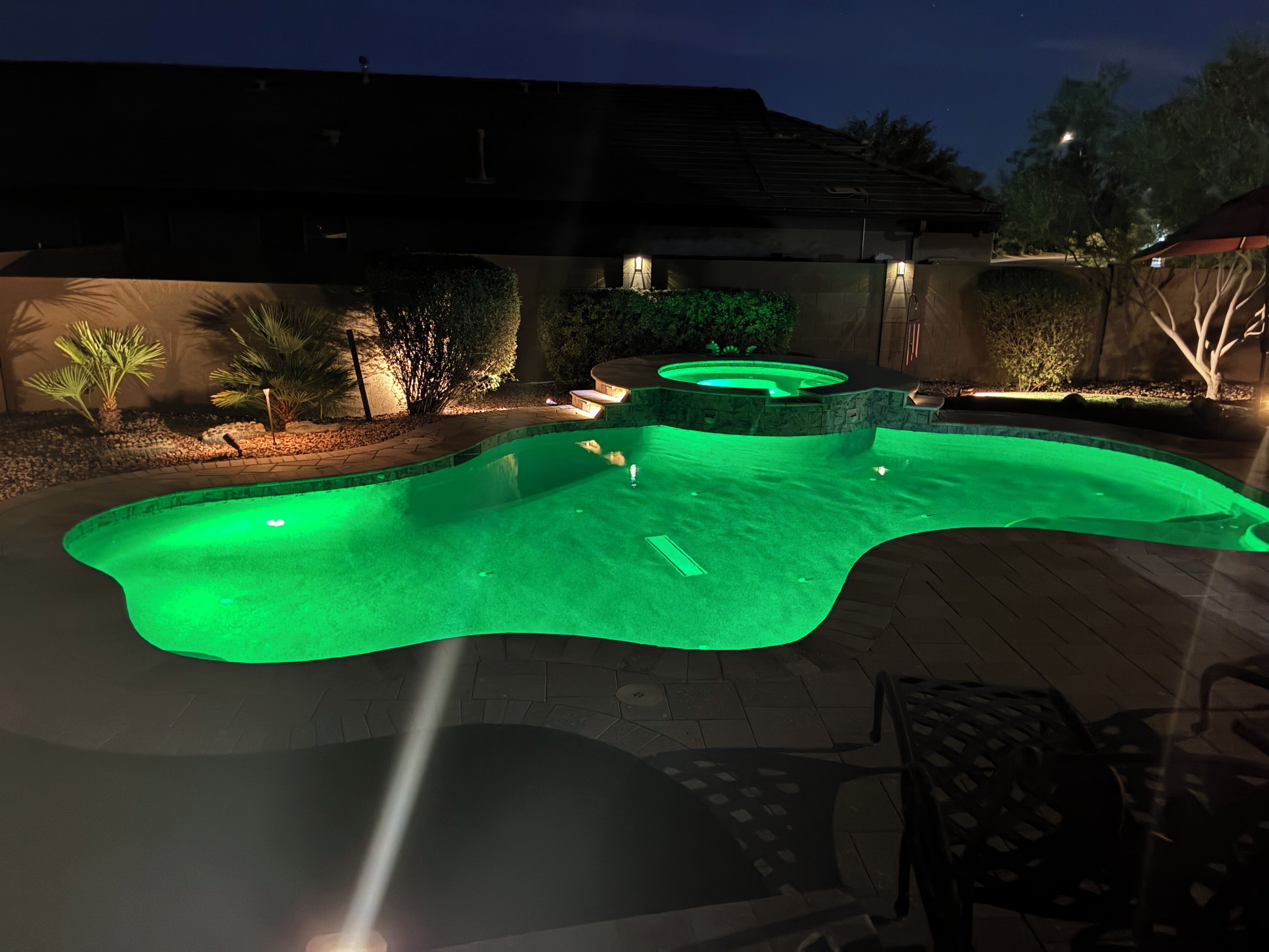 Una piscina con un jacuzzi, rodeada por un patio con sillas y un muro de piedra.