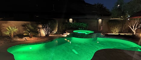 En swimmingpool med ett bubbelbad, omgiven av en uteplats med stolar och en stenmur.