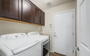 A laundry room with two white washers and dryers, wooden cabinets above, a white door, and a thermostat on the wall.
