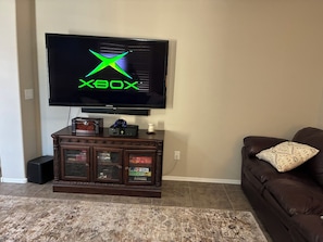 Ein Wohnzimmer mit an der Wand montiertem Fernseher, einem dunkelbraunen Unterhaltungsschrank darunter und einem braunen Ledersofa mit dekorativer Kissen.