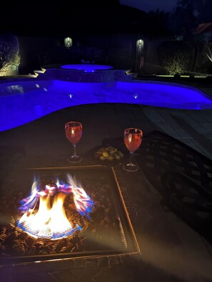 Area piscina con un elemento decorativo a fuoco e due bicchieri di bevanda rossa su un tavolo.