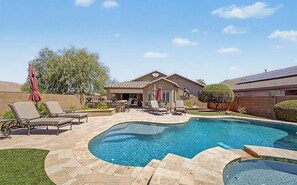 A backyard with a swimming pool, lounge chairs, and a patio area.