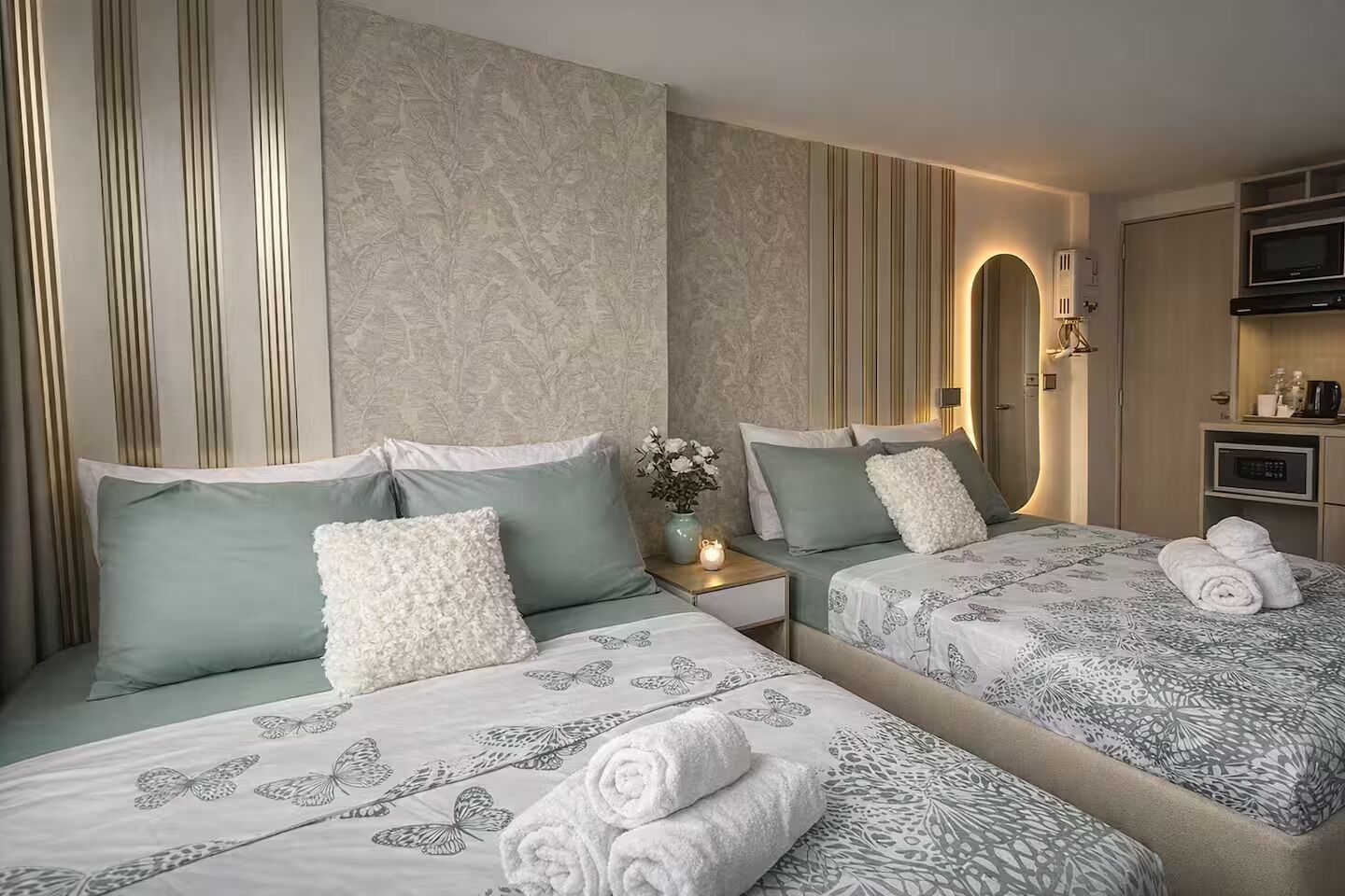 A hotel room with two beds, a nightstand, a vase with flowers, and a built-in TV.