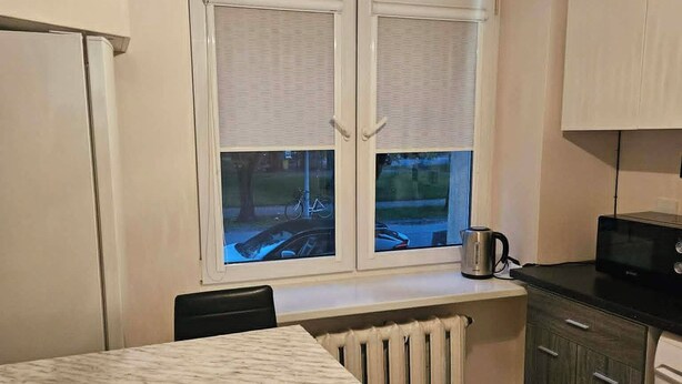Eine kleine Küche mit Esstisch, Heizkörper und einem Fenster mit Jalousien.