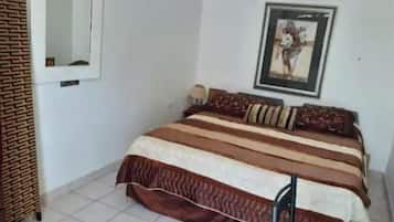 Een slaapkamer met een bed, een spiegel, een ingelijst kunstwerk en een betegelde vloer.