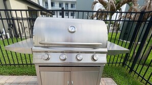 Un barbecue d’extérieur en acier inoxydable, doté de quatre brûleurs, d’un thermomètre intégré et d’une étagère latérale.