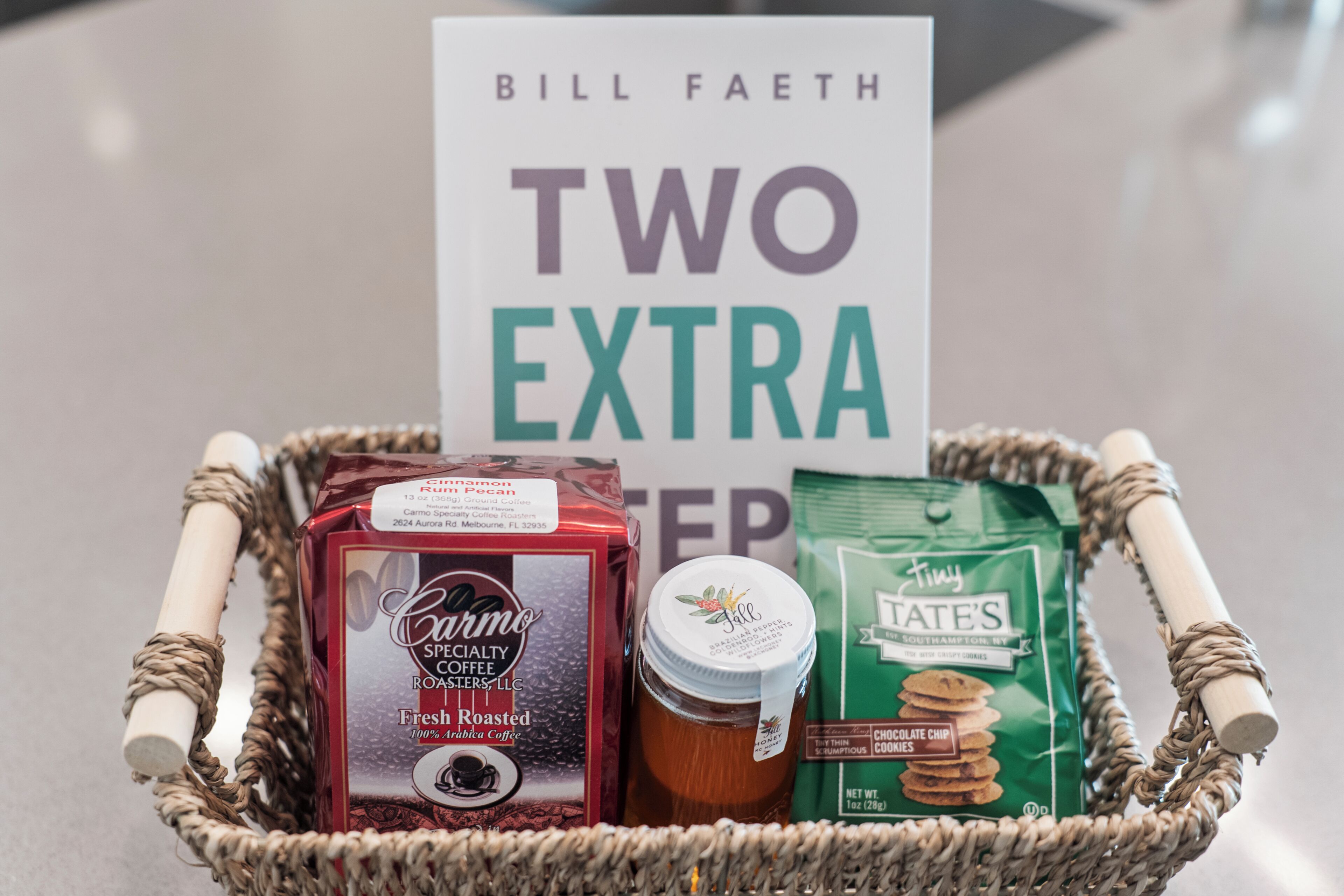 A basket containing a box of Caramo Specialty Coffee, a jar of honey, and a bag of TATE'S cookies.