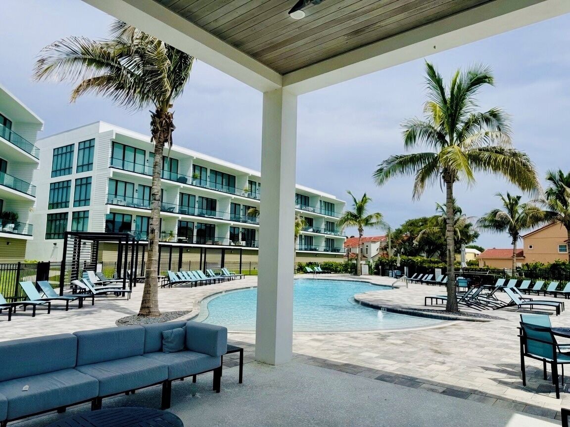 A hotel pool area with lounge chairs, palm trees, and a modern building with balconies.
