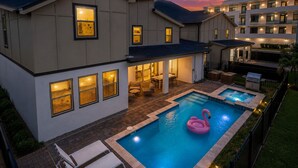 Une maison moderne à deux étages, dotée d’une piscine, de mobilier d’extérieur et d’un flotteur en forme de flamant rose.