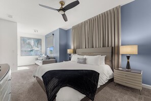 Ein Hotelzimmer mit einem großen Bett, einem Deckenventilator, einem Nachttisch mit Lampe, einem Schminktisch und einem Bild an der Wand.