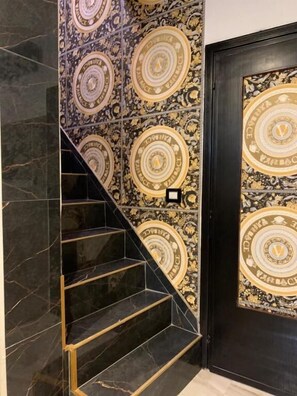 A staircase with a black and gold patterned wall, a black door with a circular emblem, and a light switch on the wall. - bristol palace (Rodigo)