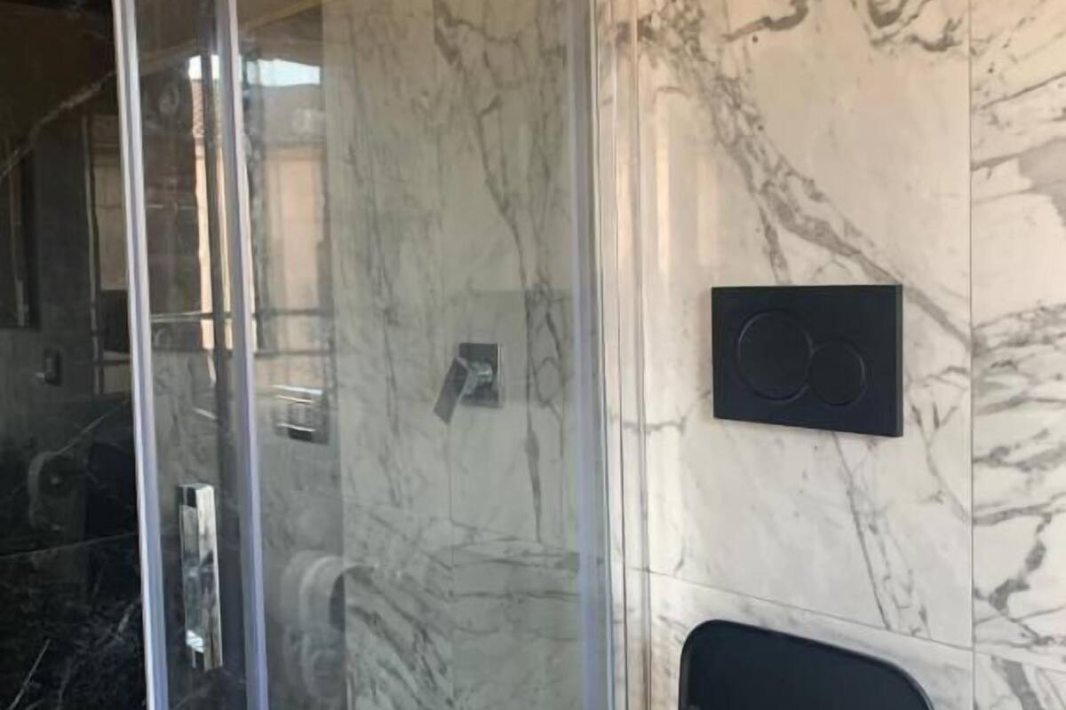 A bathroom with a glass shower enclosure, marble walls, and a black chair.