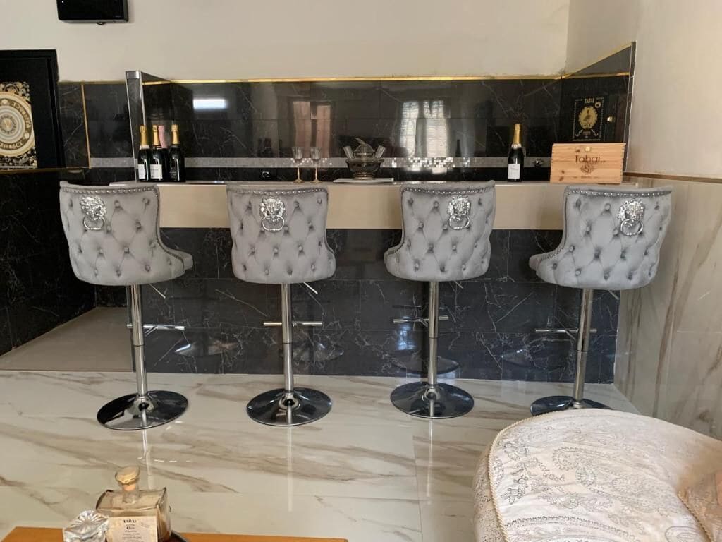 A bar area with four tufted barstools, a marble countertop, and a minibar with bottles.
