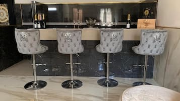 A bar area with four tufted barstools, a marble countertop, and a minibar with bottles.