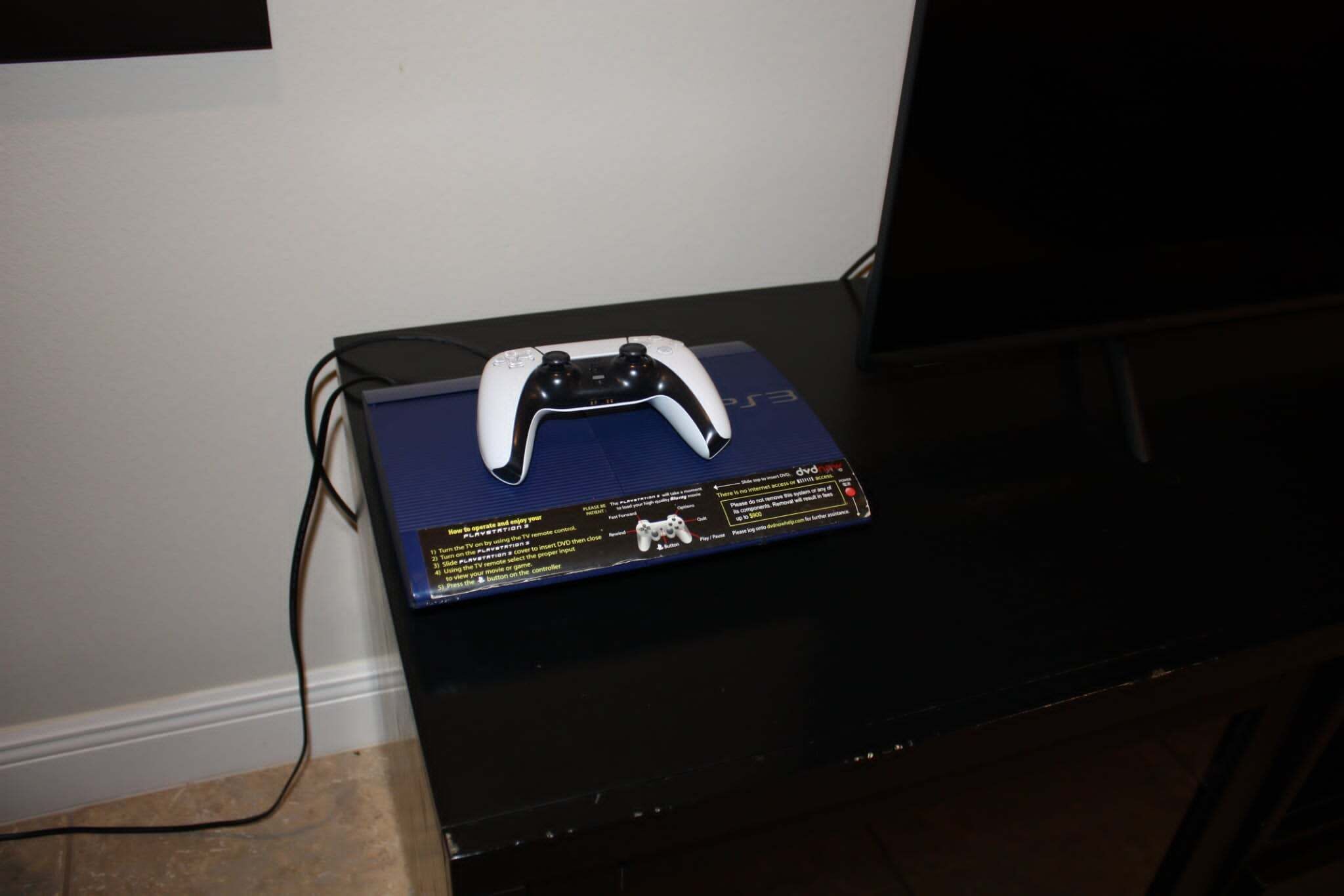 Un dispositivo electrónico negro con un control de juego encima, sobre una superficie azul.
