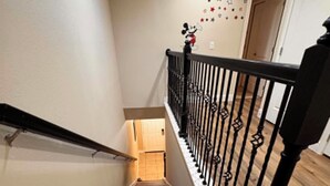 Uma escadaria com degraus de madeira e guarda-corpos de metal preto, que leva a um quarto com uma porta no topo.