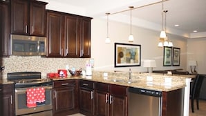 Uma cozinha com armários de madeira escura, eletrodomésticos de aço inoxidável, bancadas de granito e iluminação pendente.