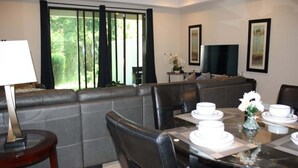 Uma sala de estar moderna com um sofá, uma mesa de jantar posta para quatro pessoas, uma TV e obras de arte emolduradas na parede.