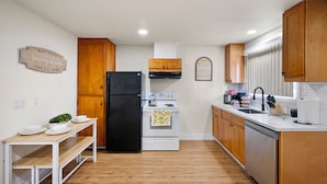 Una cocina con armarios de madera, un refrigerador negro, una estufa y una mesa de comedor con platos y una planta.
