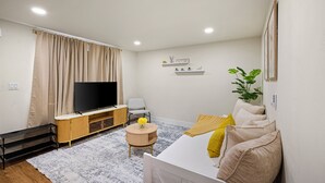 Una sala de estar moderna con un televisor de pantalla plana, un sofá con cojines, una mesita redonda con un jarrón y una planta en maceta.