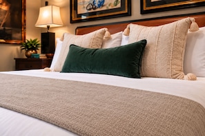 A neatly made bed with a beige blanket, a green pillow, and several other pillows with tassels. - Couples King Suite at Barefoot Resort / Private Entrance, Resort Pool, Marina (N Myrtle Beach)