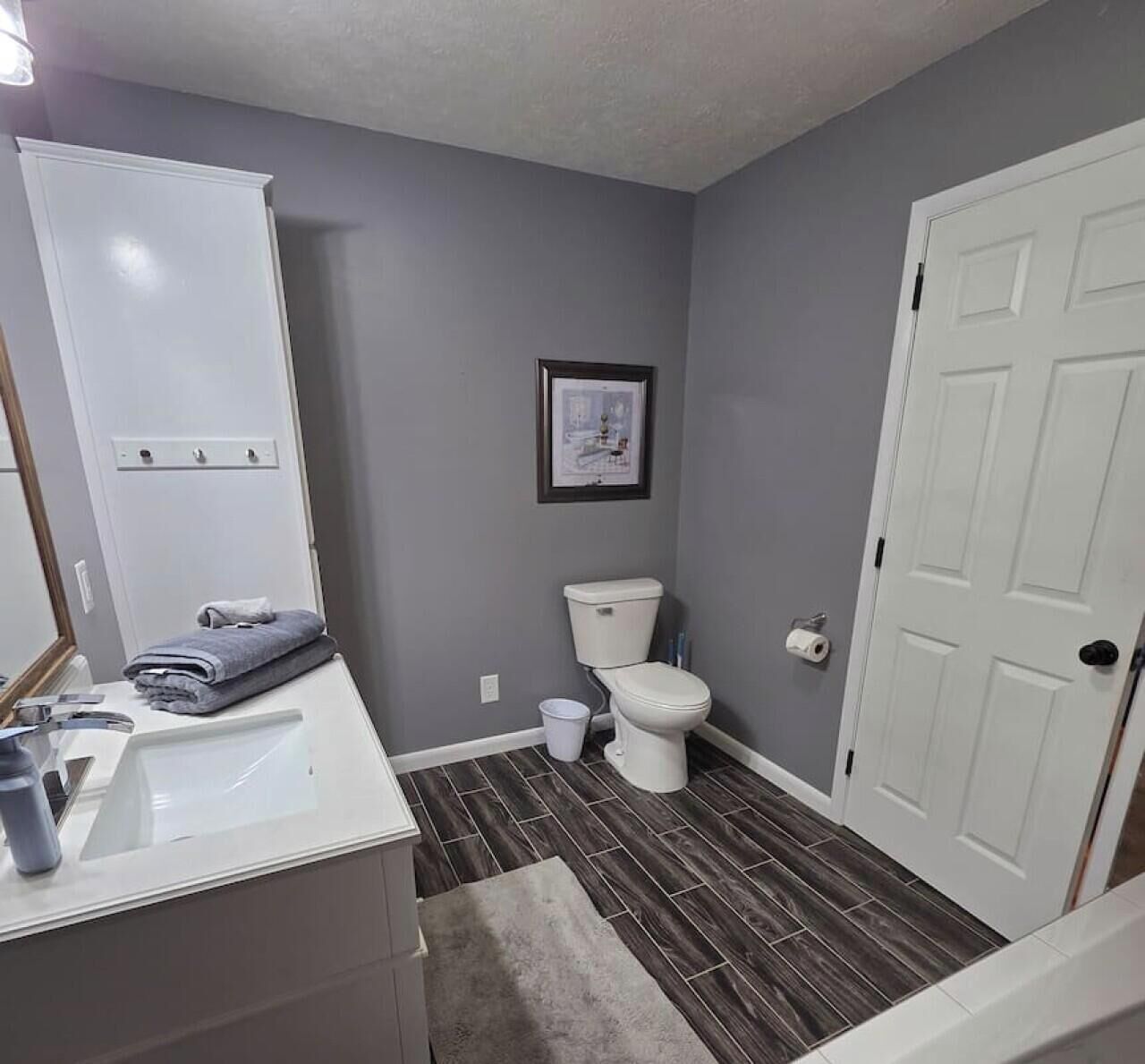 Ein Badezimmer mit einer weißen Toilette, einem Waschbecken mit Spiegel und einem gerahmten Bild an der Wand.