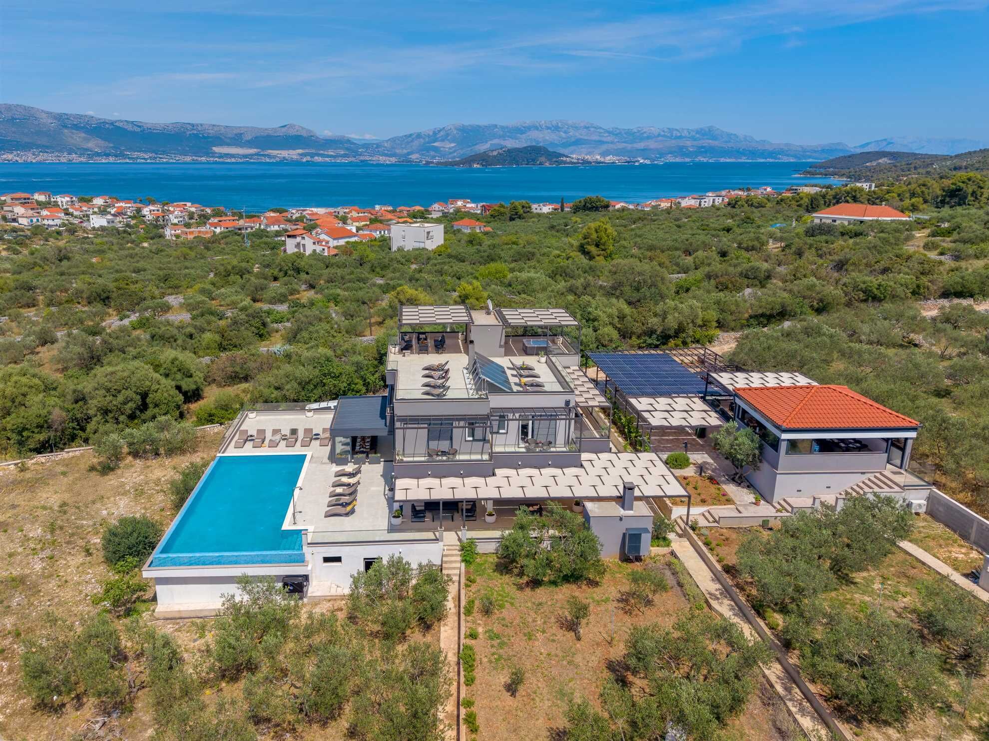 Une villa moderne dotée d’une piscine, de panneaux solaires et offrant une vue sur la mer et les montagnes.