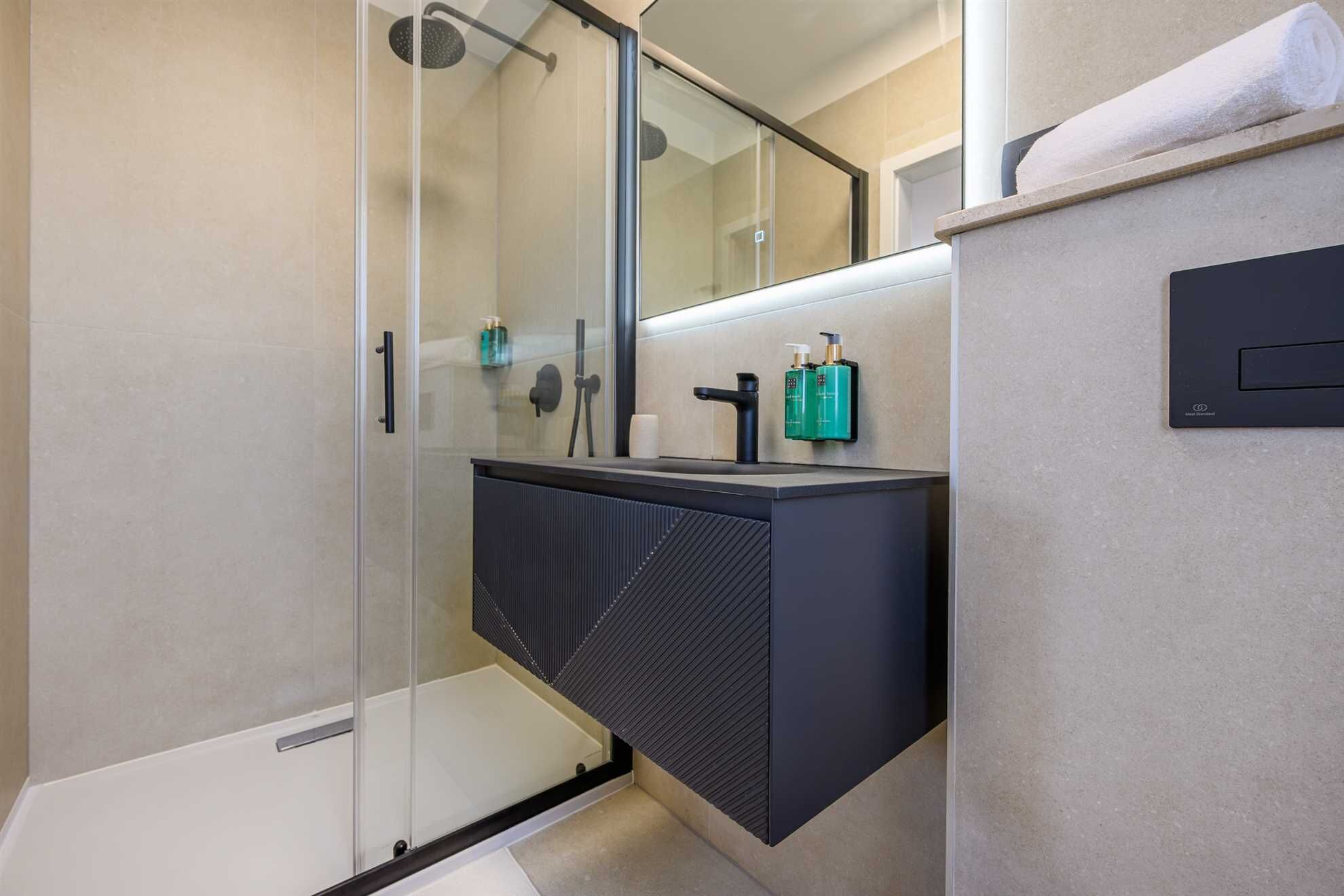 Ein modernes Badezimmer mit Duschkabine aus Glas, einem schwarzen Waschtisch und einem Handtuch an der Wand.