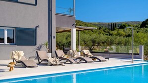A modern poolside area with lounge chairs, a clear blue pool, and a view of a hilly landscape.