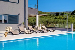 Ein moderner Poolbereich mit Liegestühlen, einem klaren blauen Pool und Blick auf eine hügelige Landschaft.