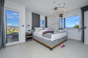 Ein modernes Schlafzimmer mit einem großen Bett, einem Schreibtisch, einem Stuhl, Blick ins Freie und einer außergewöhnlichen Deckenleuchte.