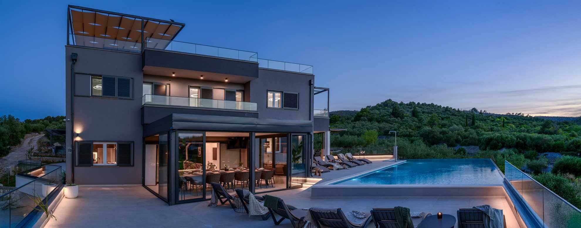 Una casa moderna de dos pisos con piscina, mobiliario exterior y vista a la vegetación circundante.