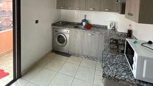 Een kleine keuken met een wasmachine, een magnetron en een gasfornuis.