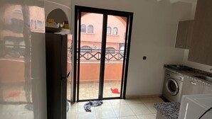 Een keuken met een wasmachine, een koelkast en een schuifdeur naar een buitenruimte.