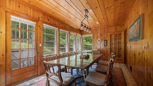 A wooden-paneled dining room with a large table and chairs, large windows, and a chandelier. - Woodlea Cottage in the Heart of the National Park (Empire)