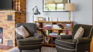 A living room with two armchairs, a bookshelf, a fireplace, and a television. - Woodlea Cottage in the Heart of the National Park (Empire)