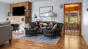A living room with a fireplace, two armchairs, a bookshelf, and a television. - Woodlea Cottage in the Heart of the National Park (Empire)