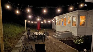 An outdoor patio with string lights, a table, chairs, and a barbecue grill. - Woodlea Cottage in the Heart of the National Park (Empire)