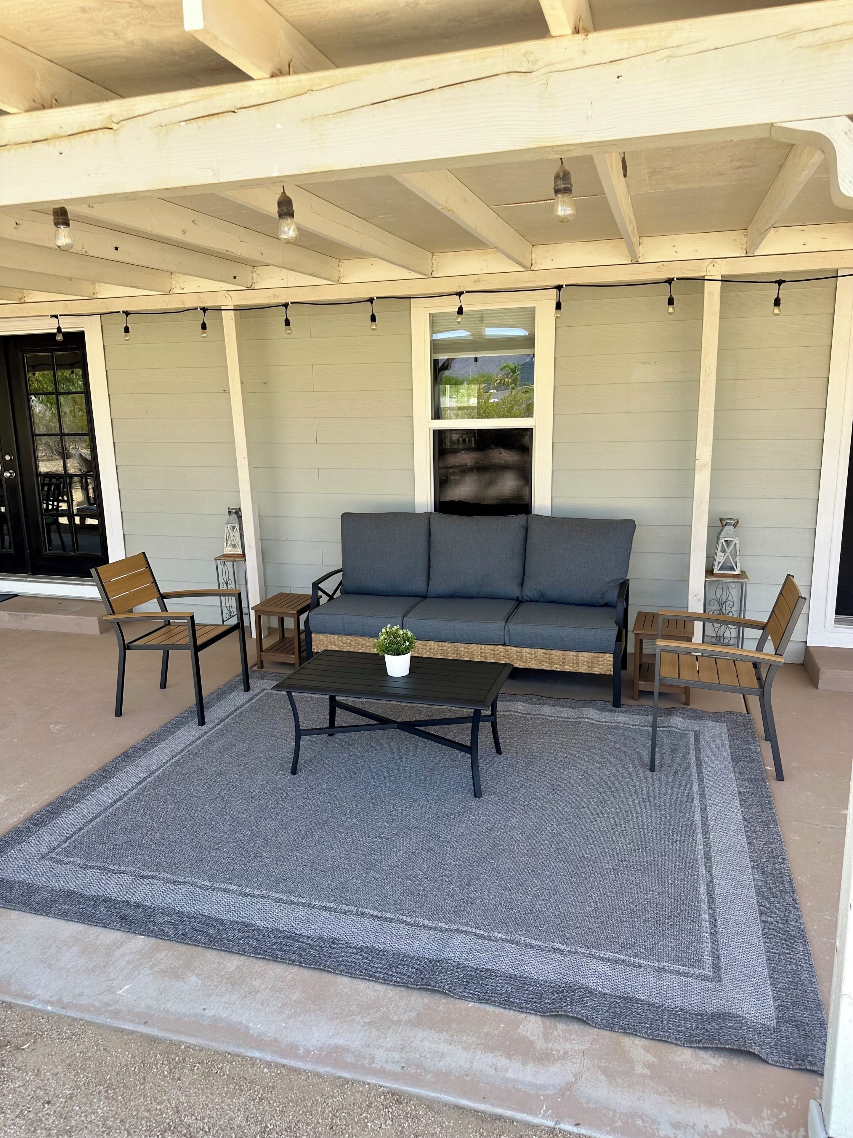 A covered outdoor seating area with a sofa, two chairs, a coffee table, and string lights.