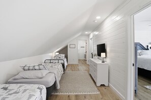 Een slaapkamer met een stapelbed, een nachtkastje met een lamp, een aan de muur bevestigde televisie en een gang die naar een andere kamer leidt.