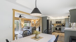 A modern kitchen with stainless steel appliances, a dining area with a checkered tablecloth, and a cozy living space with a sofa and wooden walls. - Doodle's Mountain Cape - Raystown Lake - Aunt Susie's (James Creek)