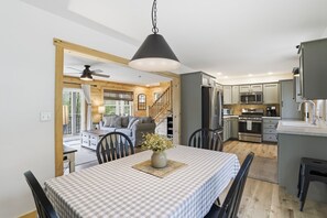 A modern kitchen with stainless steel appliances, a dining area with a checkered tablecloth, and a cozy living space with a sofa and wooden walls. - Doodle's Mountain Cape - Raystown Lake - Aunt Susie's (James Creek)